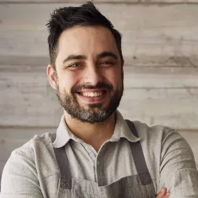 ICE Alumni David Viana smiles into the camera wearing a collared shirt and grey apron