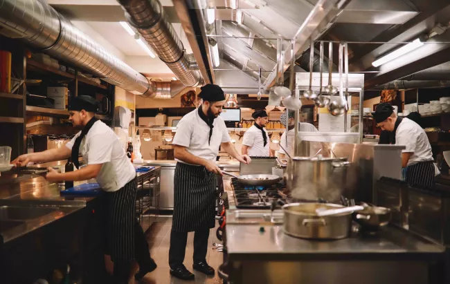 A chef stands in professional kitchen cooking on a stove